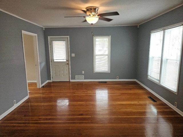 empty room with wood finished floors, visible vents, and ornamental molding