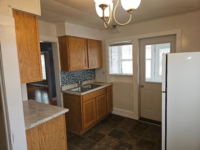 kitchen with tasteful backsplash, light countertops, brown cabinets, freestanding refrigerator, and a sink