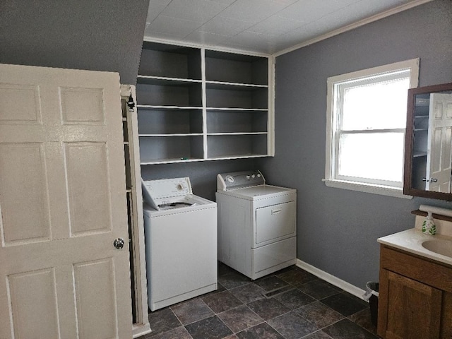 clothes washing area featuring baseboards, laundry area, stone finish floor, independent washer and dryer, and a sink