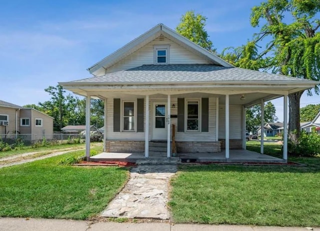 view of front of property with roof with shingles, a porch, a front yard, and fence