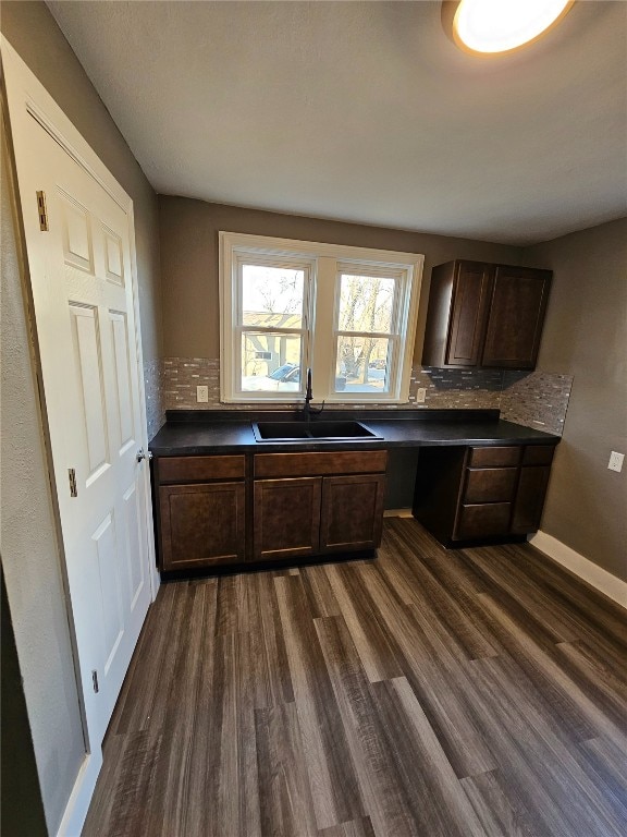 kitchen with dark wood-type flooring, a sink, dark countertops, built in desk, and decorative backsplash