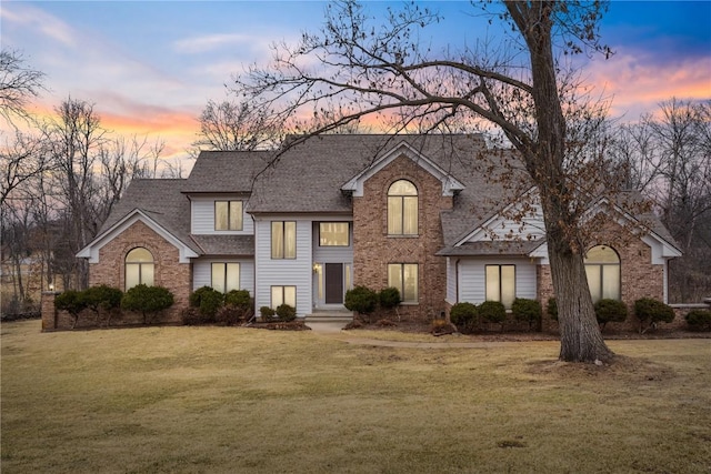 traditional-style home with brick siding, a front yard, and roof with shingles