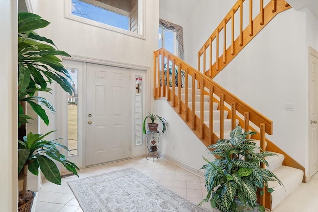 tiled foyer with stairway, a high ceiling, and baseboards