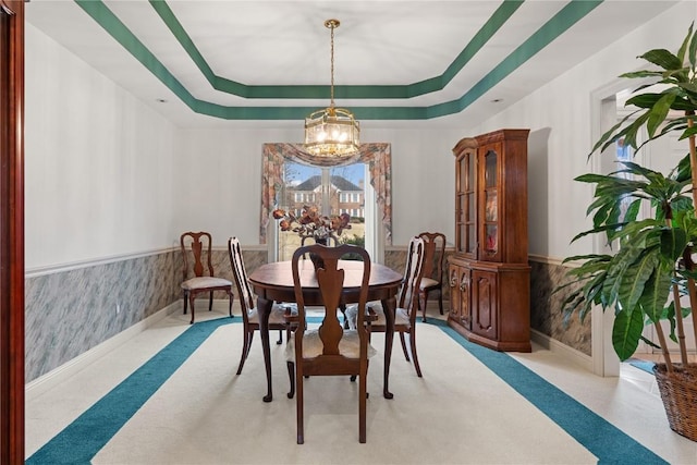 dining room featuring a notable chandelier, a wainscoted wall, a tray ceiling, and carpet floors