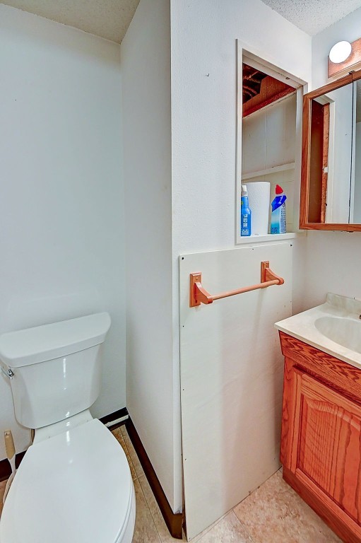 half bath with vanity, toilet, and a textured ceiling