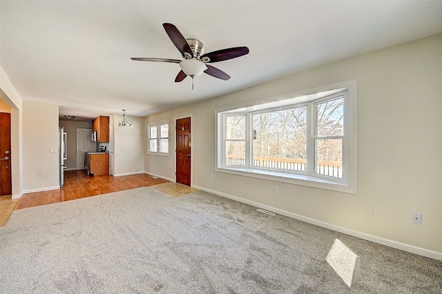 unfurnished living room with baseboards, light carpet, visible vents, and ceiling fan with notable chandelier