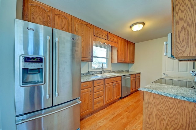 kitchen with brown cabinets, appliances with stainless steel finishes, light wood-style flooring, and a sink