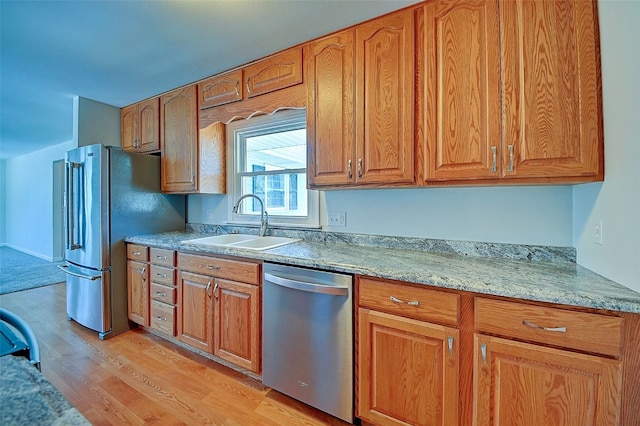 kitchen featuring a sink, light wood-style floors, appliances with stainless steel finishes, and brown cabinetry