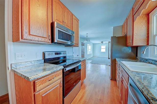 kitchen with a ceiling fan, a sink, light wood-style floors, appliances with stainless steel finishes, and brown cabinetry