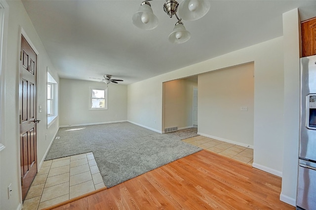 unfurnished room with a ceiling fan, baseboards, visible vents, light carpet, and light wood-type flooring