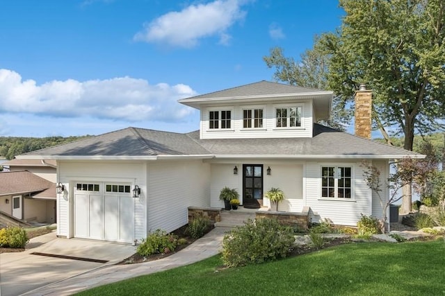 prairie-style home with driveway, roof with shingles, a front yard, an attached garage, and a chimney