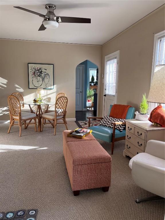 carpeted living area with arched walkways and ceiling fan