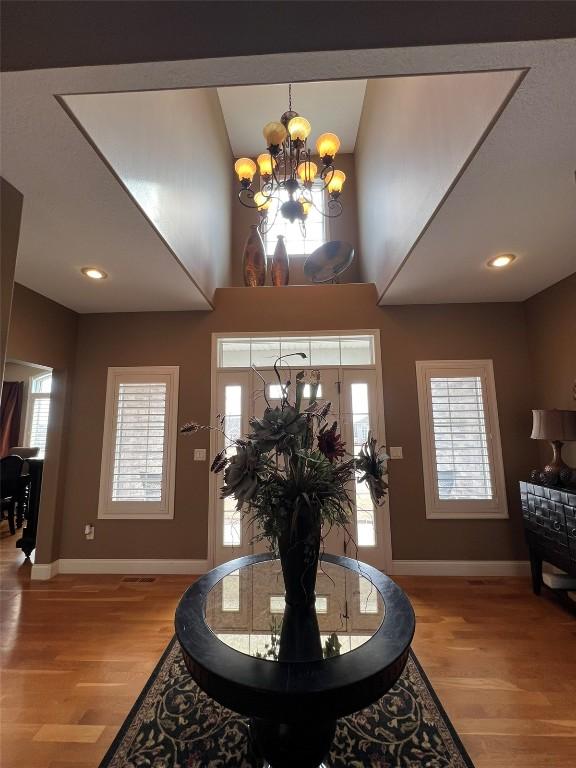 entrance foyer with baseboards, a high ceiling, an inviting chandelier, and wood finished floors