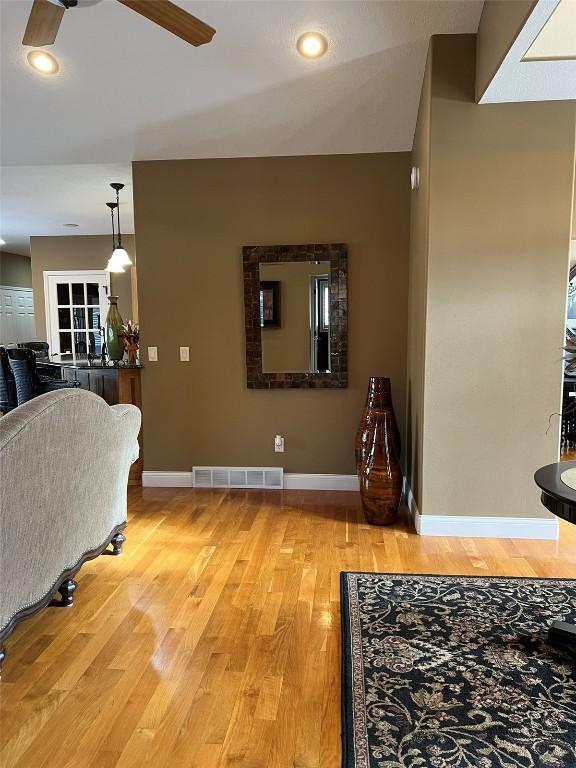 living room featuring light wood-style flooring, a ceiling fan, visible vents, and baseboards