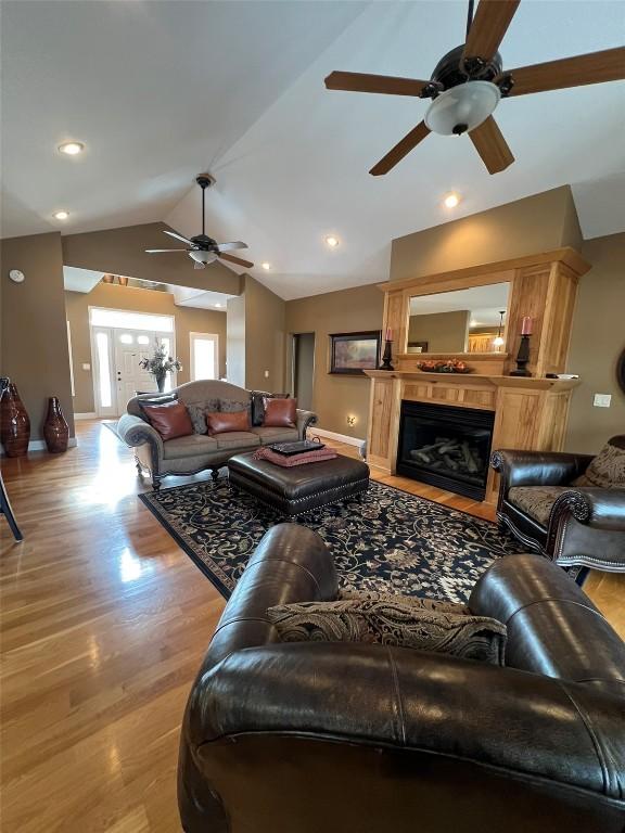 living room featuring a ceiling fan, baseboards, light wood finished floors, vaulted ceiling, and a glass covered fireplace