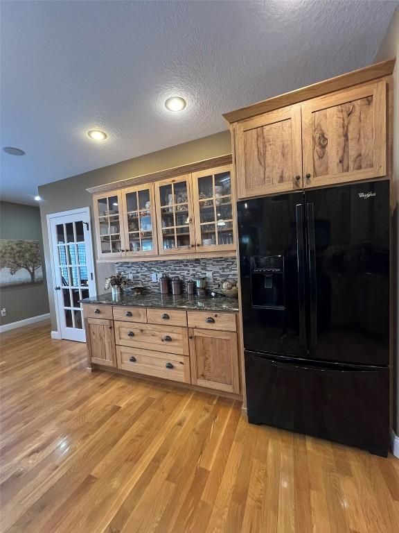 kitchen featuring tasteful backsplash, glass insert cabinets, light wood-style flooring, black refrigerator with ice dispenser, and a textured ceiling