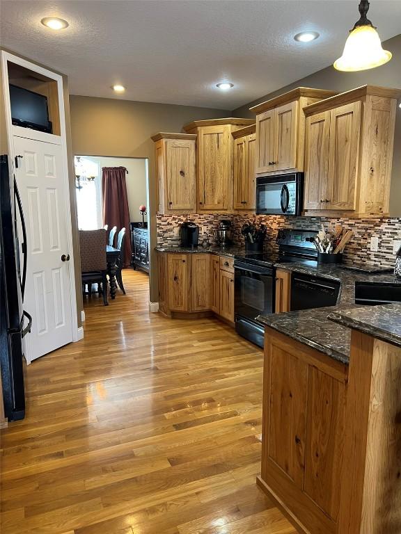 kitchen with tasteful backsplash, dark stone countertops, black appliances, and light wood-type flooring