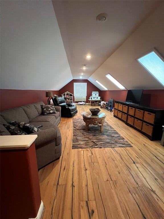 living area featuring vaulted ceiling with skylight and wood-type flooring