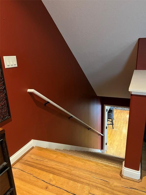 stairway with vaulted ceiling, wood finished floors, and baseboards