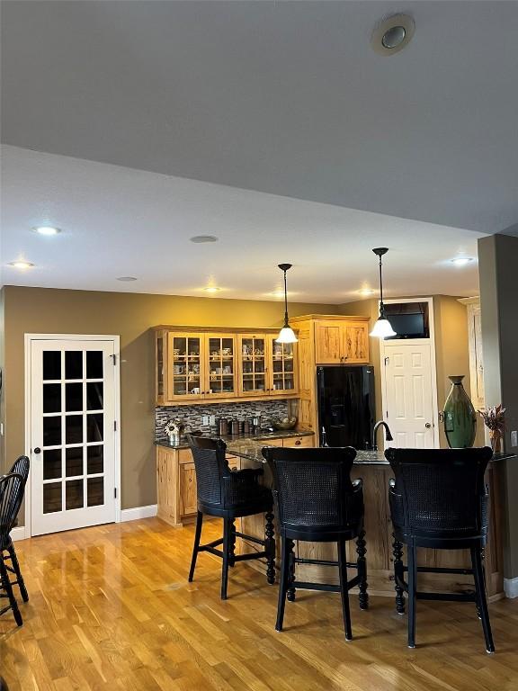 bar featuring baseboards, light wood finished floors, freestanding refrigerator, decorative light fixtures, and tasteful backsplash