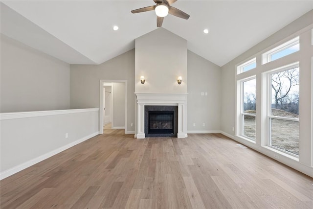 unfurnished living room with high vaulted ceiling, a ceiling fan, a glass covered fireplace, light wood-style floors, and baseboards