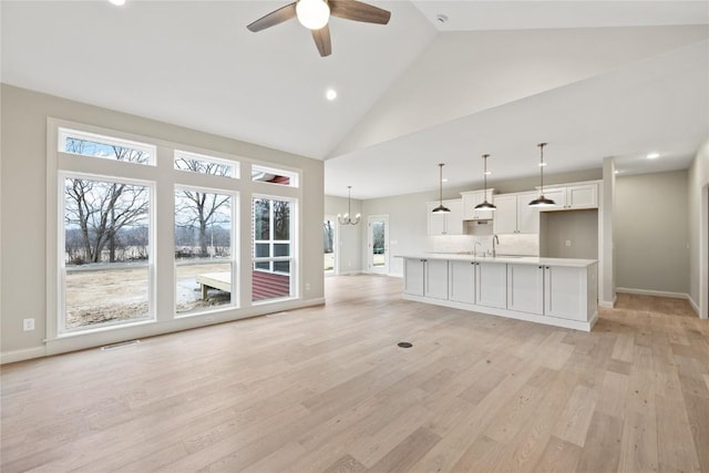 unfurnished living room with light wood-type flooring, high vaulted ceiling, a healthy amount of sunlight, and ceiling fan with notable chandelier