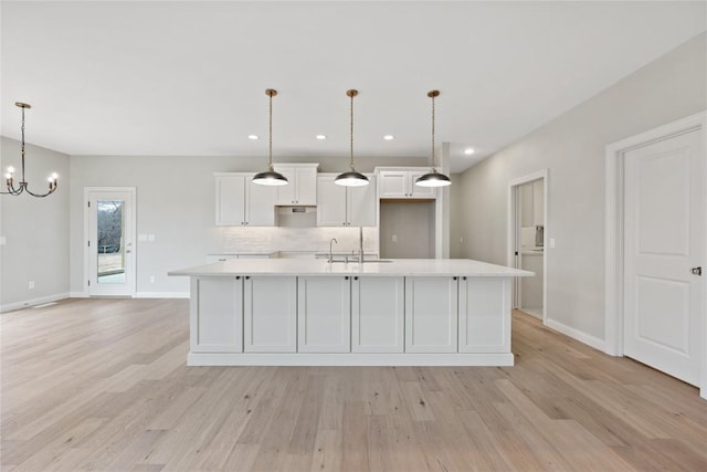 kitchen with white cabinetry, light countertops, light wood finished floors, and a large island with sink