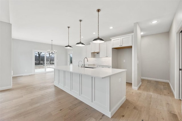 kitchen with a sink, white cabinetry, light wood finished floors, a large island with sink, and light countertops