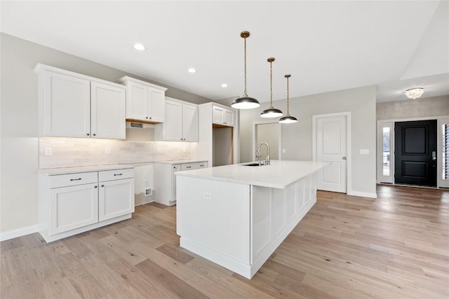 kitchen with a sink, light wood finished floors, a kitchen island with sink, and white cabinetry