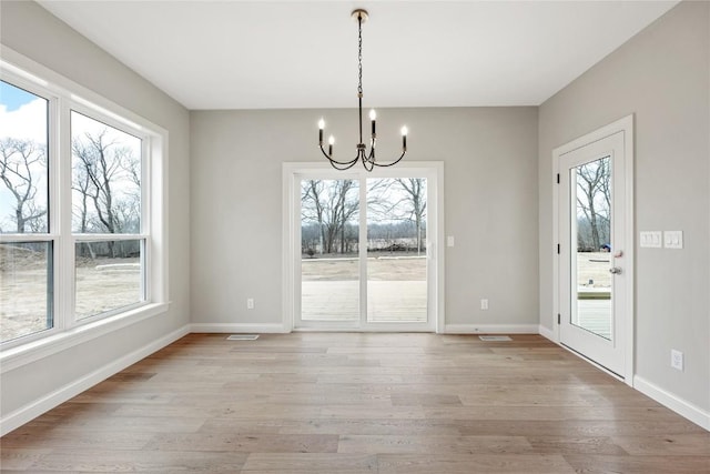 unfurnished dining area featuring a notable chandelier, a healthy amount of sunlight, and light wood-type flooring