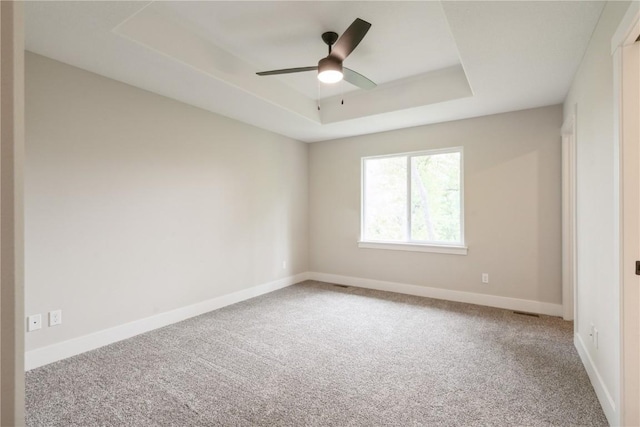 carpeted spare room featuring a raised ceiling, a ceiling fan, and baseboards