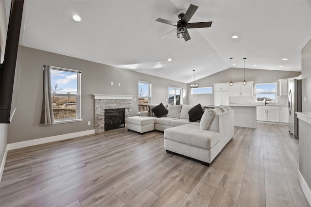 living area featuring lofted ceiling, light wood-style flooring, plenty of natural light, and a fireplace