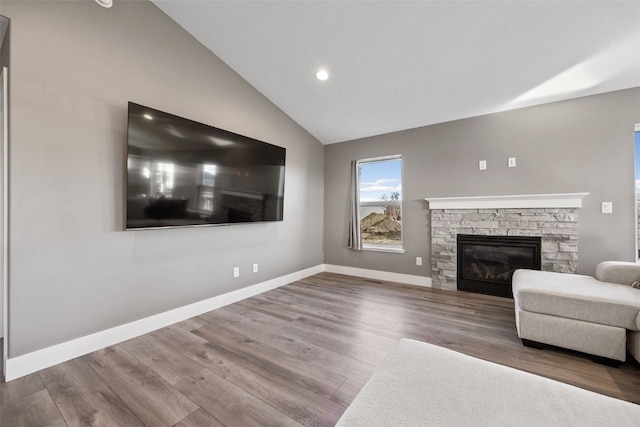 unfurnished living room with a stone fireplace, baseboards, lofted ceiling, and wood finished floors