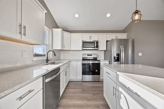 kitchen with light stone countertops, wood finished floors, a sink, vaulted ceiling, and appliances with stainless steel finishes