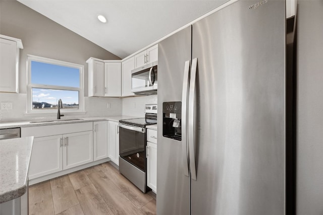 kitchen with light wood finished floors, a sink, stainless steel appliances, vaulted ceiling, and tasteful backsplash