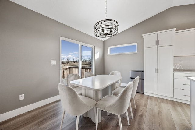 dining space featuring a chandelier, light wood-type flooring, baseboards, and vaulted ceiling