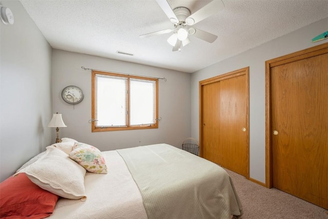 carpeted bedroom with visible vents, a textured ceiling, two closets, and ceiling fan