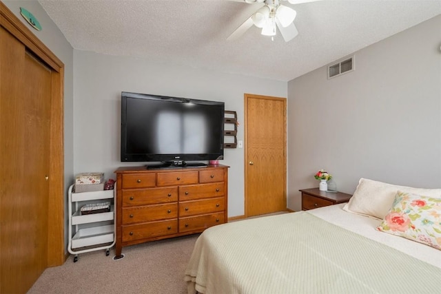 bedroom featuring visible vents, a textured ceiling, a closet, light colored carpet, and ceiling fan