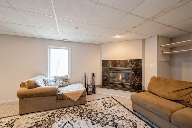 carpeted living area featuring a glass covered fireplace, baseboards, and a drop ceiling