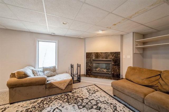 living area with a glass covered fireplace, carpet, baseboards, and a paneled ceiling