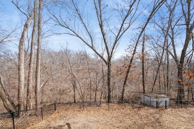 view of yard featuring an outbuilding, a forest view, and fence