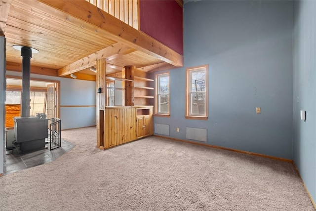 interior space featuring a wood stove, carpet flooring, wood ceiling, and visible vents