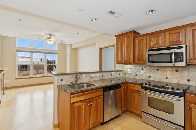 kitchen with a peninsula, brown cabinetry, appliances with stainless steel finishes, and a sink