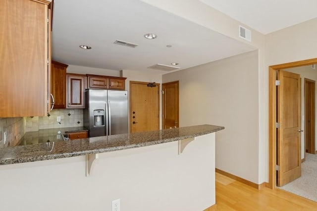 kitchen with a kitchen breakfast bar, stainless steel fridge, backsplash, and a peninsula