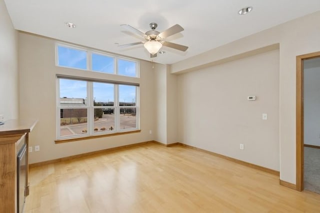 empty room featuring a ceiling fan, baseboards, and light wood finished floors