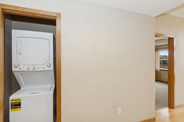 laundry area featuring light carpet, laundry area, stacked washing maching and dryer, and baseboards