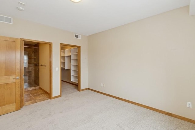 unfurnished bedroom with a spacious closet, visible vents, light colored carpet, and baseboards