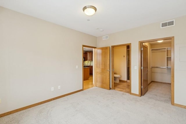 unfurnished bedroom featuring a spacious closet, light colored carpet, visible vents, and baseboards