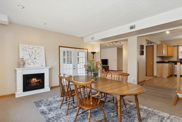 dining room featuring visible vents, a warm lit fireplace, french doors, a textured ceiling, and light colored carpet