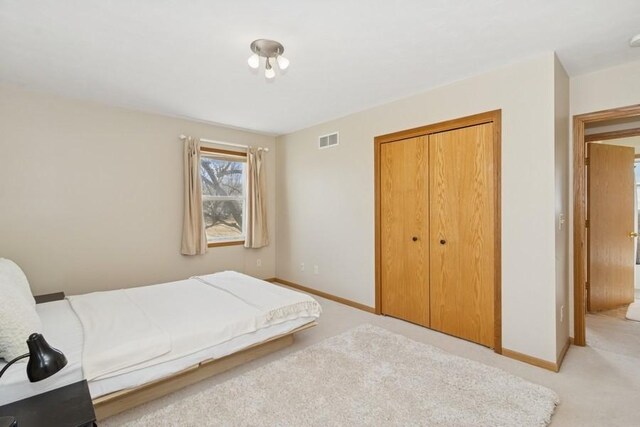 unfurnished bedroom featuring a closet, visible vents, light colored carpet, and baseboards